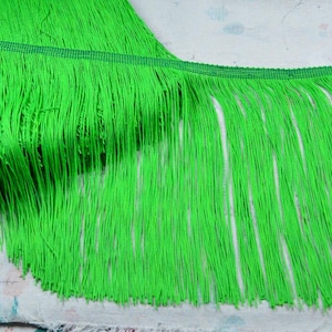 Puede incluir: Flecos de color verde brillante con una banda verde tejida en la parte superior. Los flecos están hechos de hebras largas y finas de un color verde vibrante. Este adorno es adecuado para proyectos de manualidades y diseño.