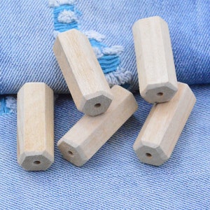 May include: Six unfinished wooden hexagonal beads, each with a hole drilled through the center. The beads are arranged on a blue denim fabric background.