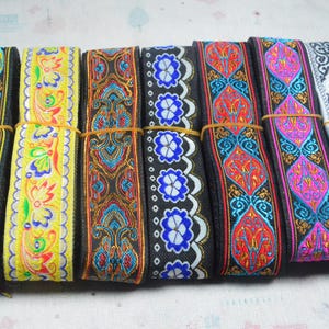 Könnte beinhalten: Sieben Rollen dekoratives Stoffband, die nebeneinander angeordnet sind. Jede Rolle weist unterschiedliche Stickmuster in verschiedenen Farben auf, darunter Gelb, Schwarz, Weiß, Blau, Rot und Pink, die mit dünnen Gummibändern fixiert sind.