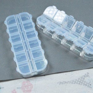 Peut inclure: Deux piluliers en plastique transparent avec plusieurs compartiments. Chaque pilulier a une forme rectangulaire avec un couvercle &agrave; charni&egrave;re pour chaque compartiment. Con&ccedil;u pour ranger et organiser de petits objets comme des pilules ou des perles.
