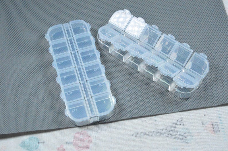 Peut inclure: Deux piluliers en plastique transparent avec plusieurs compartiments. Chaque pilulier a une forme rectangulaire avec un couvercle &agrave; charni&egrave;re pour chaque compartiment. Con&ccedil;u pour ranger et organiser de petits objets comme des pilules ou des perles.