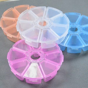 May include: A set of four circular plastic storage containers, each featuring eight individual wedge-shaped compartments with hinged lids. The containers are translucent and come in clear, light blue, light pink, and light orange colors.