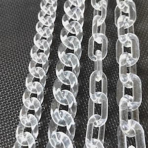 Könnte beinhalten: Nahaufnahme von mehreren transparenten Acrylkettensträngen. Die Ketten bestehen aus ineinandergreifenden ovalen und rechteckigen Gliedern. Die Ketten werden vor einem dunklen, strukturierten Hintergrund dargestellt. Die Ketten sind transparent und reflektieren Licht.