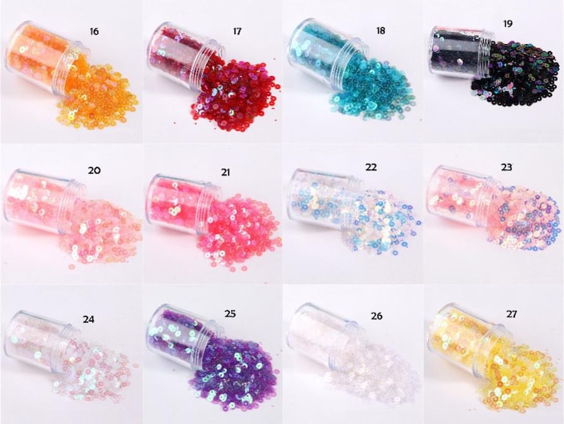 May include: A collection of small, clear jars, each filled with colorful sequins. The sequins are in various colors, including orange, red, teal, black, pink, light blue, and purple. The jars are tipped over, spilling the sequins.