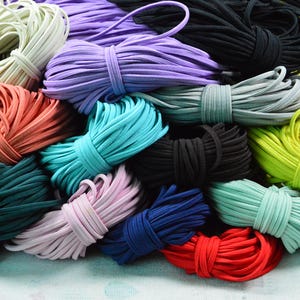 May include: A collection of colorful elastic cords in various hues, including purple, teal, black, and red. The cords are bundled and tied, showcasing a variety of colors and textures. These elastic cords are suitable for crafting and DIY projects.
