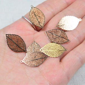 May include: A collection of delicate leaf-shaped charms in various metallic finishes, including gold, copper, and bronze. Each charm features intricate vein detailing and a small loop for attachment, perfect for jewelry making or crafting projects.