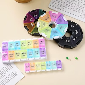 Puede incluir: Una colección de pastilleros coloridos en varias formas. Hay dos organizadores circulares, uno negro y otro con colores del arcoíris, y dos organizadores rectangulares. Cada compartimento está etiquetado con los días de la semana.
