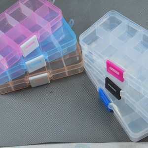 Könnte beinhalten: Mehrere transparente Kunststoff-Aufbewahrungsboxen mit mehreren Fächern. Die Boxen sind in Rosa-, Blau- und Orangetönen gehalten und haben weiße, rosa, schwarze und blaue Verschlüsse. Geeignet zum Organisieren kleiner Gegenstände.