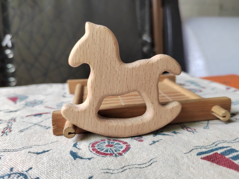 May include: A wooden rocking horse toy, made of light brown wood, with a simple design. The horse is sitting on a bamboo tray.