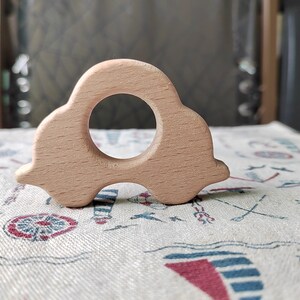 May include: A light brown wooden toy car with a round hole in the middle. The toy is on a white fabric with a blue and red pattern.