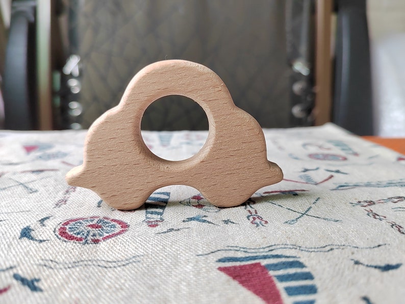May include: A light brown wooden toy car with a round hole in the middle. The toy is on a white fabric with a blue and red pattern.