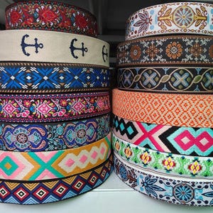 Könnte beinhalten: Stapel dekorativer Bandrollen in verschiedenen Farben und Mustern. Designs umfassen florale, geometrische und nautische Themen. Die Bänder sind aus Stoff und eignen sich für Bastelarbeiten und Verzierungen.
