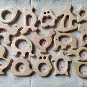 May include: Set of 16 wooden teethers in various animal shapes, including a bird, penguin, elephant, camel, chicken, owl, and turtle. Each teether has a hole in the center for a baby to hold and chew on.