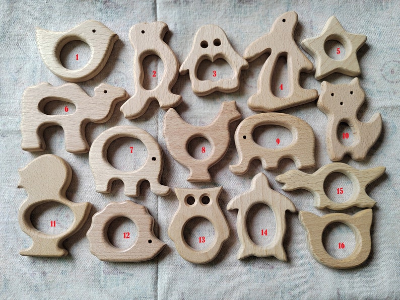 May include: Set of 16 wooden teethers in various animal shapes, including a bird, penguin, elephant, camel, chicken, owl, and turtle. Each teether has a hole in the center for a baby to hold and chew on.