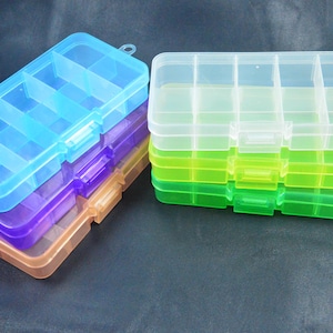 Puede incluir: Un conjunto de cajas de almacenamiento rectangulares de plástico con múltiples compartimentos internos. Las cajas están apiladas en dos columnas y presentan colores translúcidos que incluyen azul, morado, naranja, transparente, amarillo y verde.