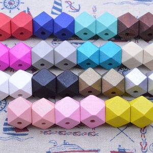 May include: Rows of colorful wooden beads in various colors, including red, pink, blue, and yellow. The beads are geometric in shape, with multiple facets and a hole drilled through the center for stringing. The beads are arranged in pairs, showcasing the range of colors available.