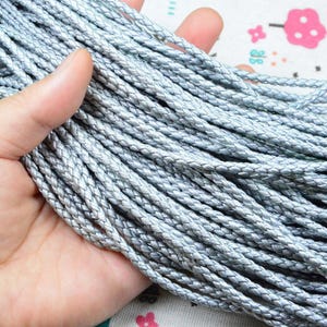 May include: A bundle of metallic silver braided cord featuring a tight, uniform weave. The cord has a smooth, reflective surface and a consistent cylindrical shape, presented as a collection of multiple strands gathered together in a thick bunch.