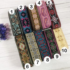Op de afbeelding: Een verzameling van tien decoratieve linten met diverse geborduurde patronen. De linten hebben ontwerpen in kleuren als zwart, bruin, roze, rood, blauw en goud. De patronen omvatten bloemen-, geometrische en paisley-motieven, geschikt voor knutselen en versieringen.