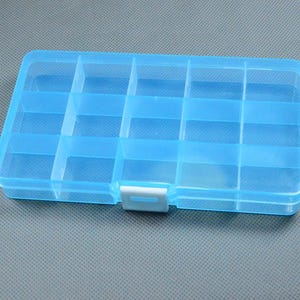 Puede incluir: Un organizador de plástico azul claro con múltiples compartimentos. La caja rectangular tiene una tapa con bisagras y un cierre blanco. El interior está dividido en varias secciones cuadradas pequeñas, ideal para guardar objetos pequeños.