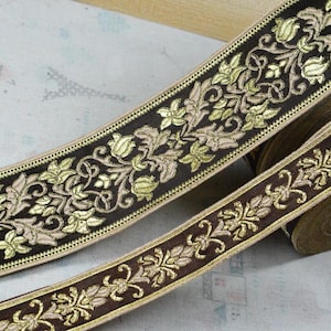 Peut inclure: Un rouleau de ruban en tissu marron foncé orné d'un motif floral brodé complexe en fil doré métallique et beige clair. Ce ruban décoratif présente un design botanique répétitif avec des feuilles et des fleurs stylisées sur toute la longueur.