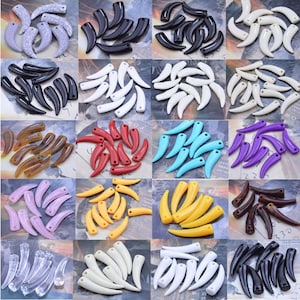 Può includere: Una collezione di perline a forma di corno di vari colori. Le perline sono disposte in un motivo a griglia, mostrando colori come bianco, nero, rosso, giallo, blu, viola e marrone. Le perline sembrano essere fatte di un materiale lucido.