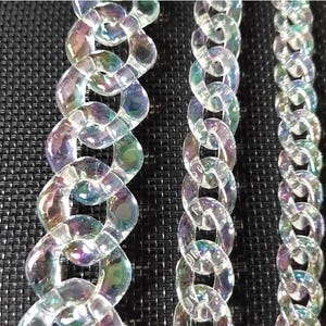 May include: Three strands of iridescent, clear plastic chain. The links are oval-shaped and reflect a rainbow of colors. The chains are displayed against a black, textured background.