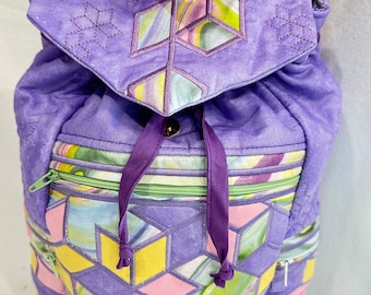 May include: Purple quilted backpack with a geometric pattern in shades of pink, yellow, and green. The backpack has a drawstring closure and two zippered pockets.