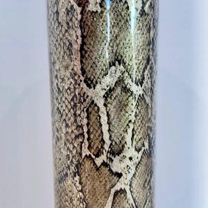 May include: A tall, clear tumbler with a snakeskin pattern. The pattern is a light brown and black color.