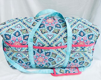 May include: A blue and pink patterned duffel bag with a detachable shoulder strap. The bag has two zippered pockets on the front.
