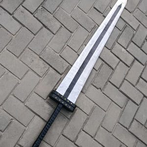 May include: A large, two-handed sword with a white blade, black accents, and a black handle. The sword has a rectangular crossguard and is lying on a gray brick surface.