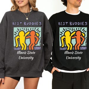May include: Two sweatshirts with the text "Best Buddies" and a graphic of two figures holding hands. The text "Illinois State University" is below the graphic. One sweatshirt is gray and the other is black.