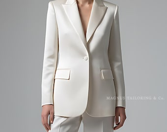May include: Ivory satin suit featuring a tailored blazer with a single-button closure and two front pockets. The suit includes matching wide-leg trousers. The text "MAGNES TAILORING & Co." is visible on the right side.