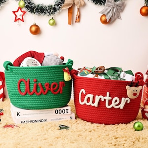 May include: Two Christmas-themed rope baskets, one green with "Oliver" in red, the other red with "Carter" in white. Both are filled with gifts and decorations, perfect for holiday storage. Festive and functional.