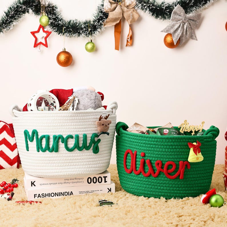 May include: Two woven rope baskets, one white and one green, are filled with Christmas decorations. The white basket has the name "Marcus" in green letters, and the green basket has the name "Oliver" in red letters. A festive holiday scene.