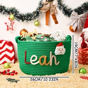 May include: A green woven basket with the name "Leah" in colorful letters. The basket is 10.23 inches wide and 7.48 inches tall, with a Santa Claus applique. The basket is filled with Christmas-themed items.