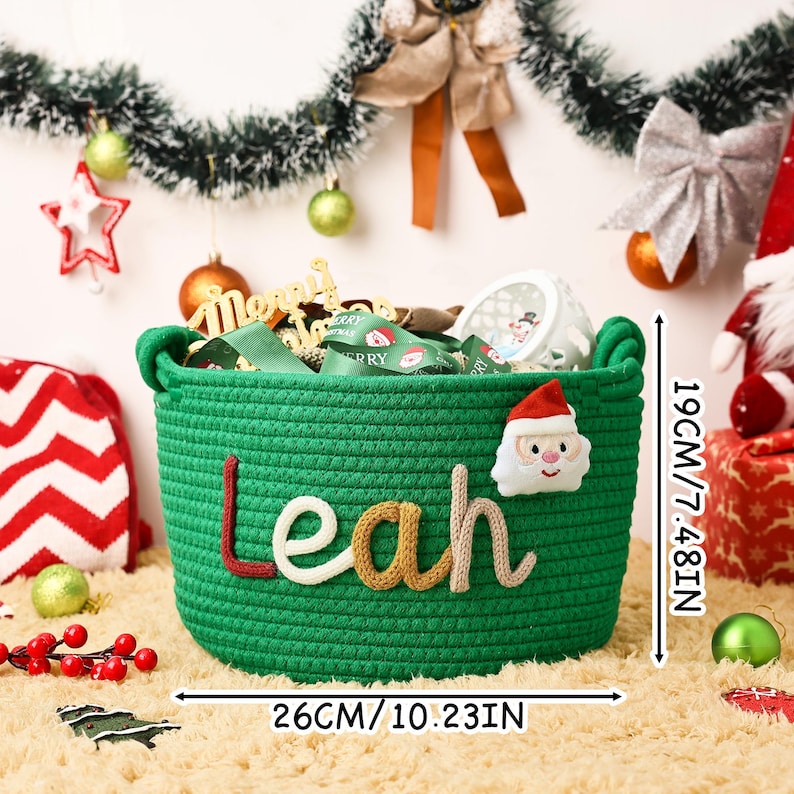 May include: A green woven basket with the name "Leah" in colorful letters. The basket is 10.23 inches wide and 7.48 inches tall, with a Santa Claus applique. The basket is filled with Christmas-themed items.
