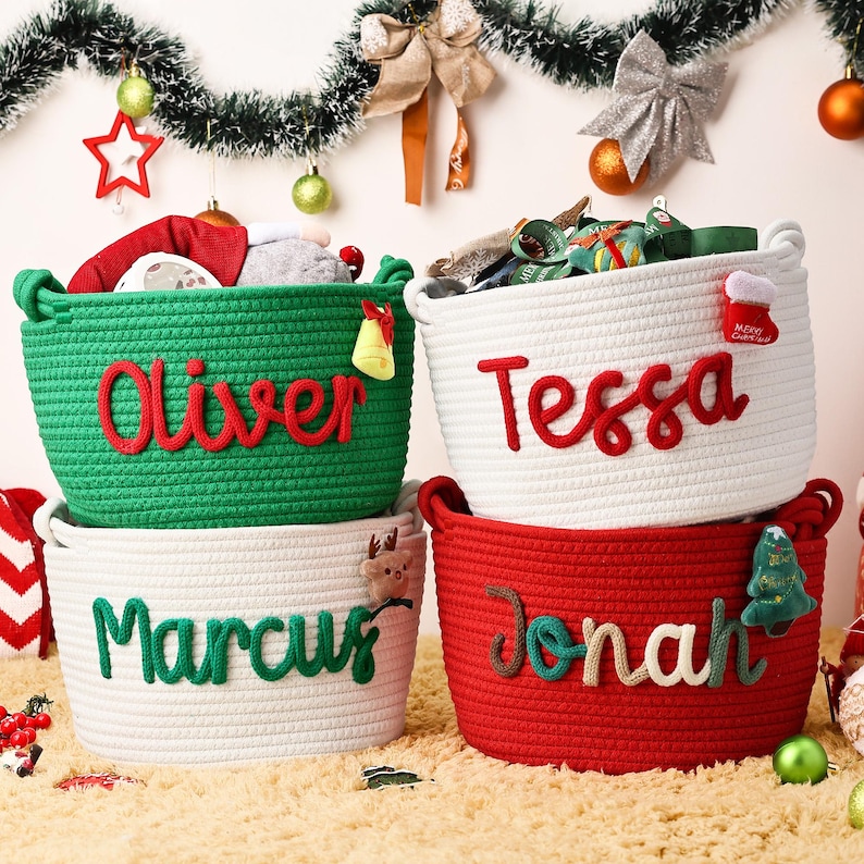May include: Four woven rope baskets in green, white, and red, each with a name in a contrasting color: "Oliver", "Tessa", "Marcus", and "Jonah". The baskets are decorated with Christmas-themed embellishments and filled with gifts.