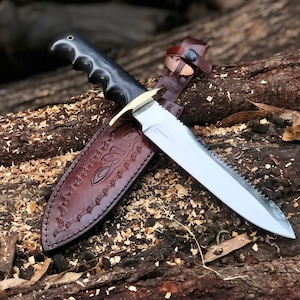 May include: A black handled knife with a serrated blade and a leather sheath. The sheath has a decorative design and the word "OSLO" embossed on it.