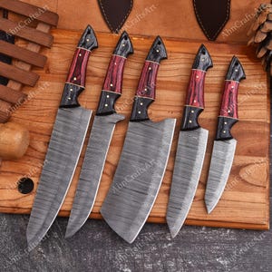 May include: A set of five kitchen knives with Damascus steel blades featuring a wavy pattern and handles made of black and red wood with brass rivets. The knives vary in size and shape, including a large chef knife, a cleaver, and smaller utility blades.