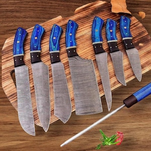 May include: A set of eight kitchen knives with blue and black handles, displayed on a wooden cutting board. The blades have a patterned design. A sharpening steel with a matching blue handle is also included.