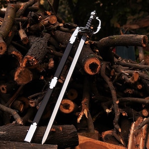 May include: A decorative sword with a silver blade and a black handle, resting against a pile of wood logs. The sword's handle has intricate detailing, and the scabbard is black with silver accents. The background is a natural setting with various wood pieces.
