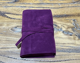 Può includere: Un astuccio arrotolabile in camoscio viola intenso con una chiusura a laccio in camoscio abbinata avvolta attorno al centro. L'accessorio rettangolare ha una consistenza morbida e opaca ed è fissato da una sottile striscia dello stesso materiale.