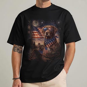 May include: Black t-shirt featuring a patriotic design with a brown dog wearing sunglasses and a bandana, set against an American flag and desert landscape. The graphic includes fireworks and a full moon.