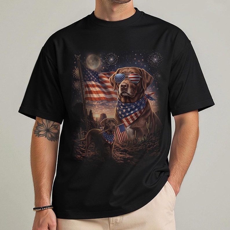 May include: Black t-shirt featuring a patriotic design with a brown dog wearing sunglasses and a bandana, set against an American flag and desert landscape. The graphic includes fireworks and a full moon.
