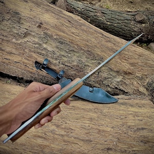 A handmade machete knife displayed with its leather sheath. Crafted from 1095 steel with a full tang for strength, this large knife is suitable for survival and camping. Makes a thoughtful and rugged gift for husbands, fathers, or any outdoorsman who appreciates handmade craftsmanship.