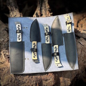 Close side view of the natural white handle chef knife set displaying the smooth carbon steel blades and ergonomic natural material handles placed neatly in a leather roll kit. This handcrafted 5 pcs kitchen knife collection is made for daily cooking, slicing, chopping and food prep. Ideal gift idea for him or her on anniversaries, birthdays or holidays,