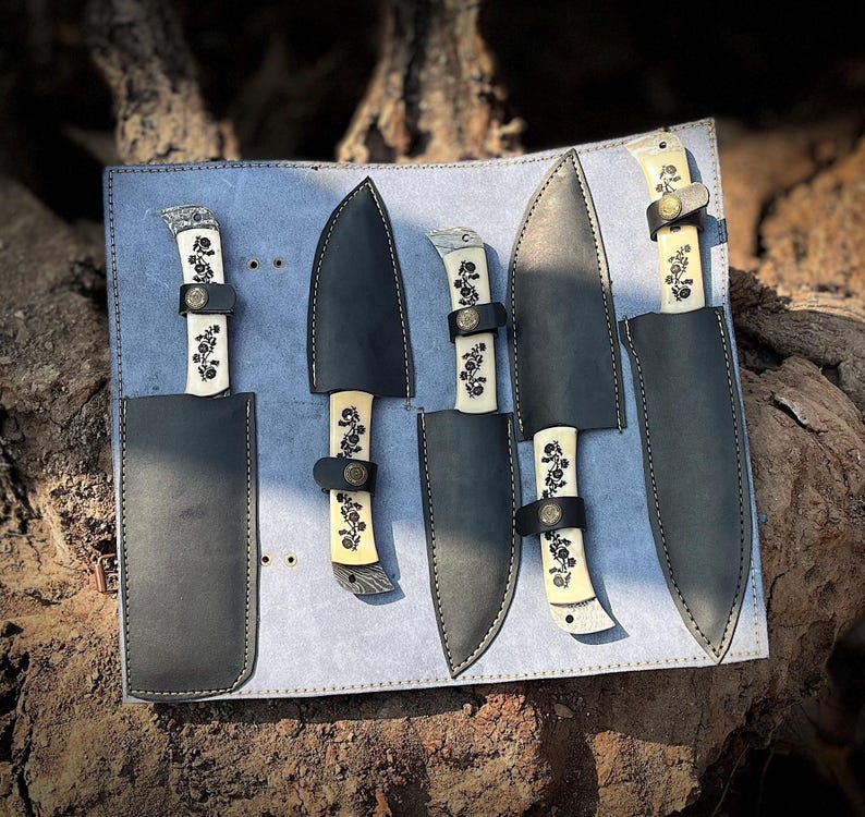 Close side view of the natural white handle chef knife set displaying the smooth carbon steel blades and ergonomic natural material handles placed neatly in a leather roll kit. This handcrafted 5 pcs kitchen knife collection is made for daily cooking, slicing, chopping and food prep. Ideal gift idea for him or her on anniversaries, birthdays or holidays,