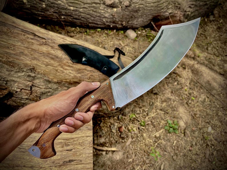 This full tang camping knife features a wide 1095 steel blade for heavy-duty outdoor use. Designed for bushcraft, hiking, and chopping, this machete-style knife is a great option for serious campers and survivalists. A personalized, handmade tool that also makes a unique gift for dads and outdoor lovers.