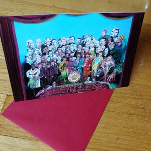 May include: A greeting card featuring a colorful illustration of a large group of people, including the Beatles, in front of a stage curtain. The card has the word "Beatles" printed in red at the bottom.
