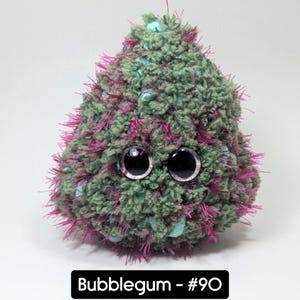 May include: A handmade, plush toy in the shape of a teardrop. The toy is green with pink accents and large, googly eyes. The text "Bubblegum - #90" is displayed in a black rectangle at the bottom.
